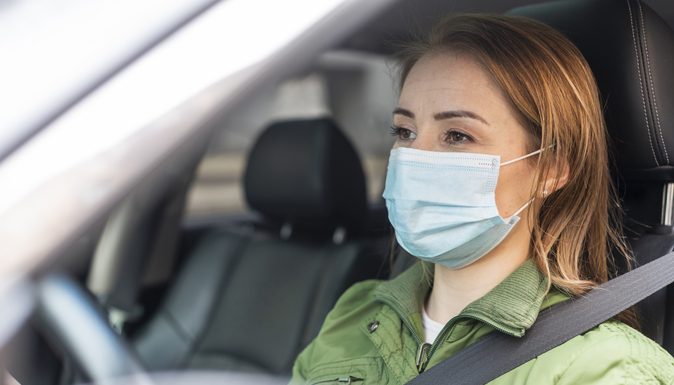 Mulher dirigindo o seu carro usando máscara de proteção